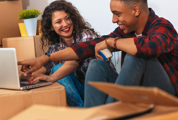 Hispanic couple sets up internet on a laptop in their new house surrounded by moving boxes.